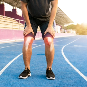 A man with knee discomfort on a running track, representing the effects of osteoporosis