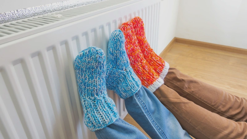 Two pairs of feet resting on a home radiator to warm up on a cold day.