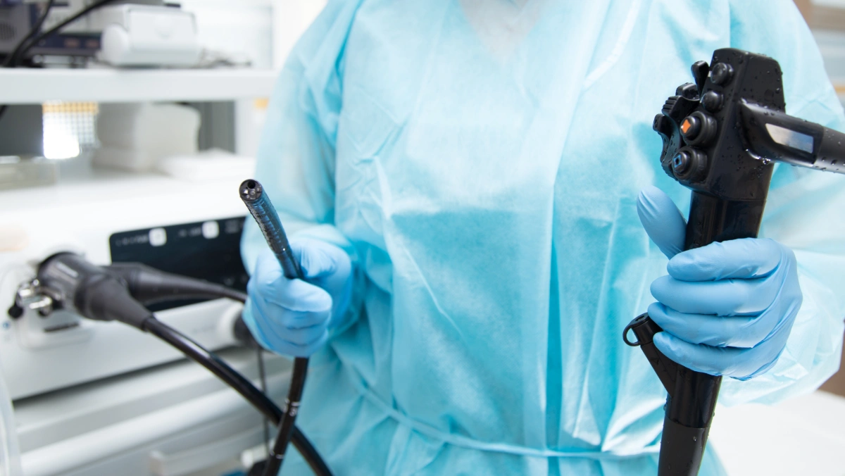 Doctor in a blue surgical gown holds an endoscope, illustrating differences between a colonoscopy and Cologuard screening.