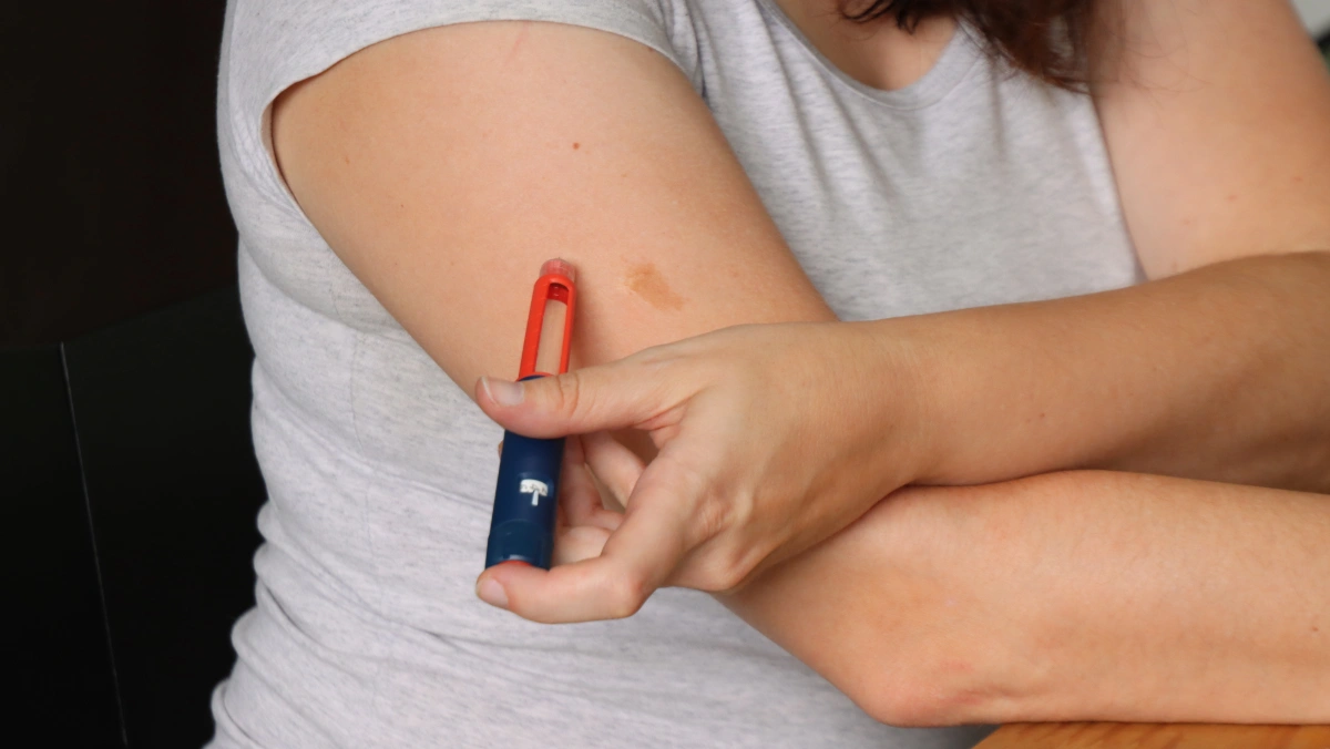 Woman using an insulin pen to inject medication into her upper arm, illustrating diabetes care and California’s CalRx insulin plan.