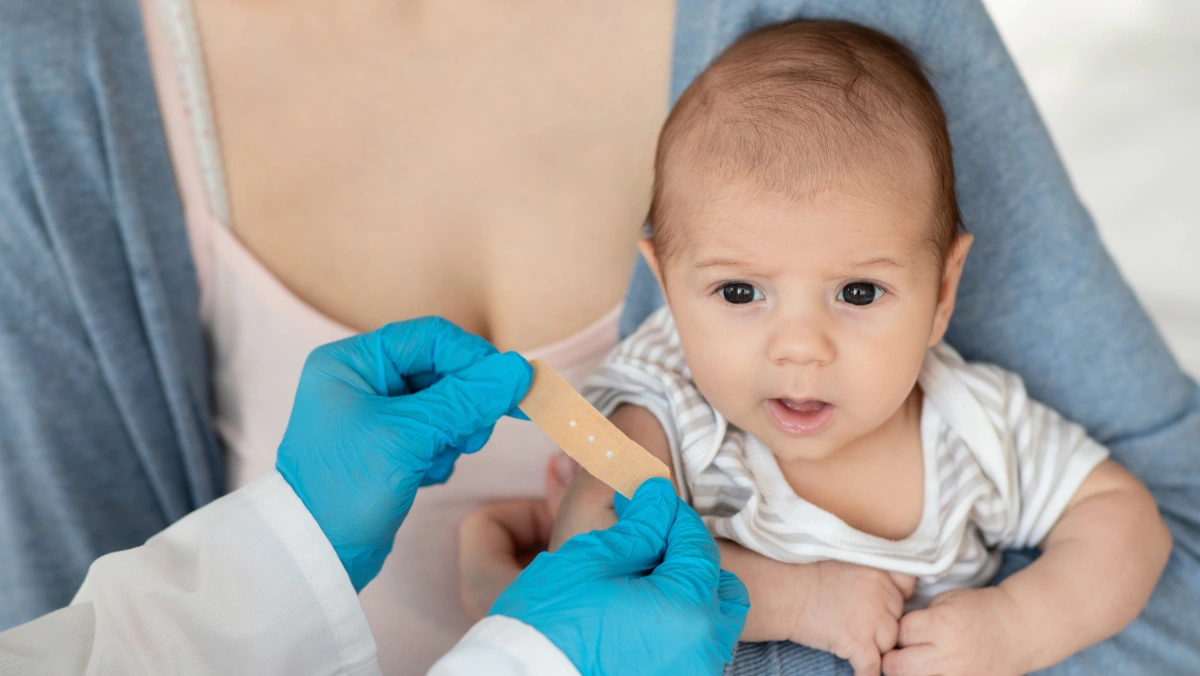 Mother holds her newborn as a doctor applies a bandage after vaccination, illustrating changes to hepatitis B vaccine guidance.