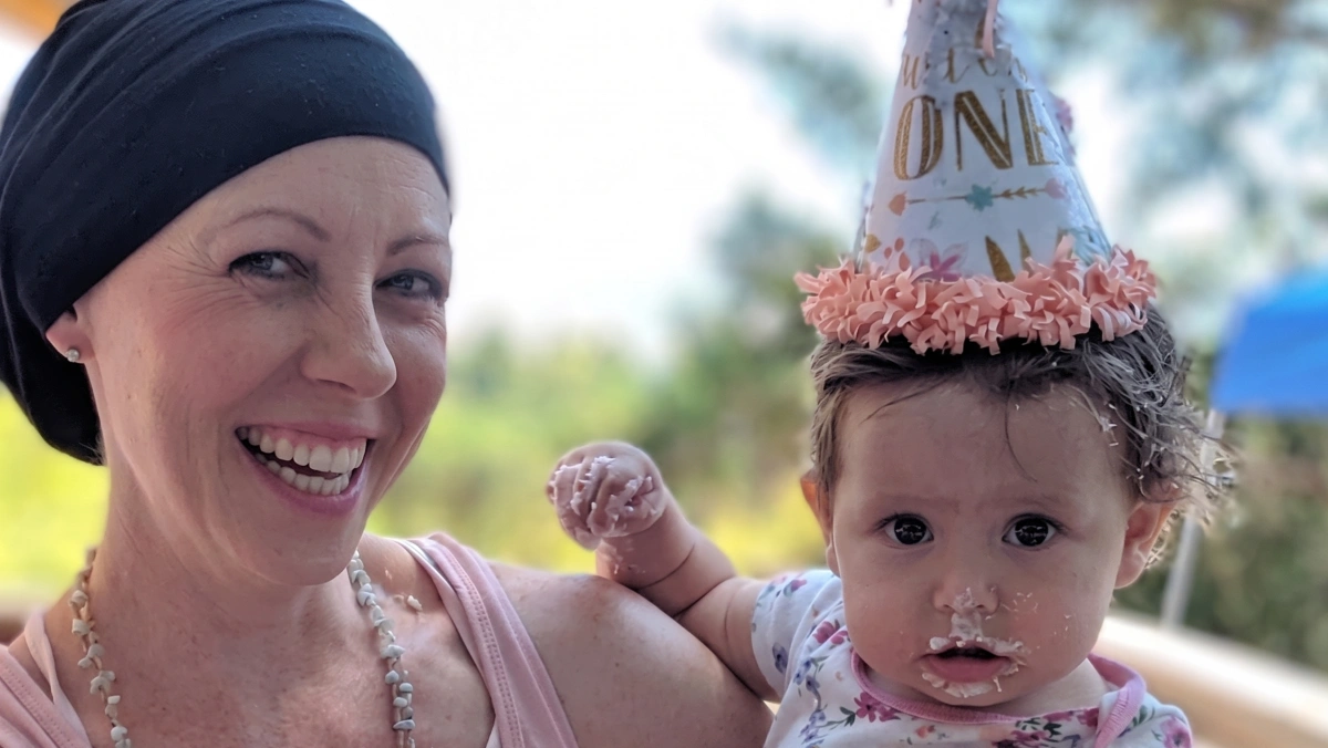 Breast cancer survivor Heather smiles with her young child in a birthday hat, celebrating life after treatment at Gregory Rhodes MD Cancer Center.