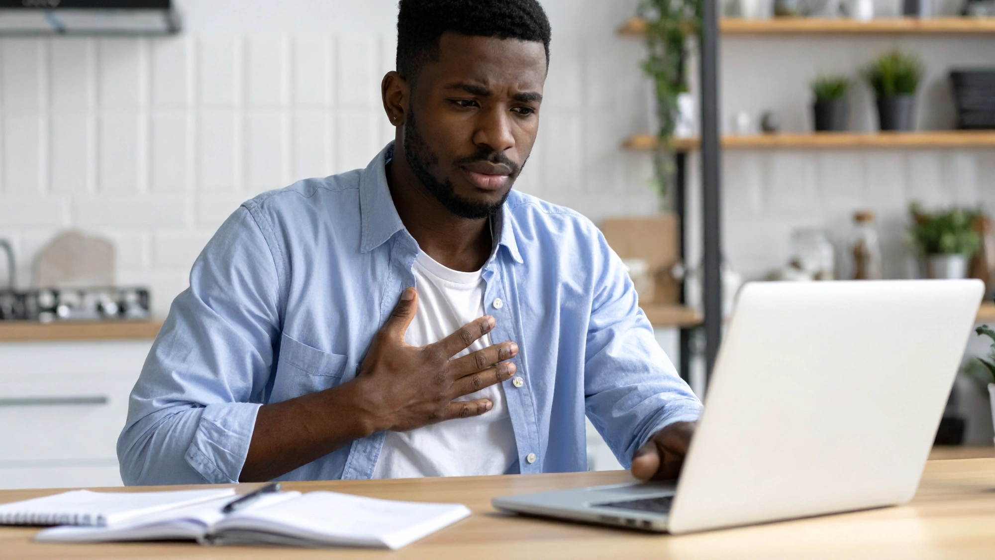 Young adult sitting at a desk with a hand near their chest, representing the rise of heart disease in younger adults.