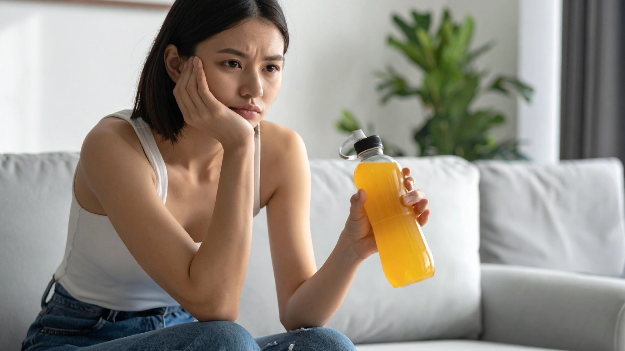 Young woman holding an electrolyte drink while recovering from a hangover.