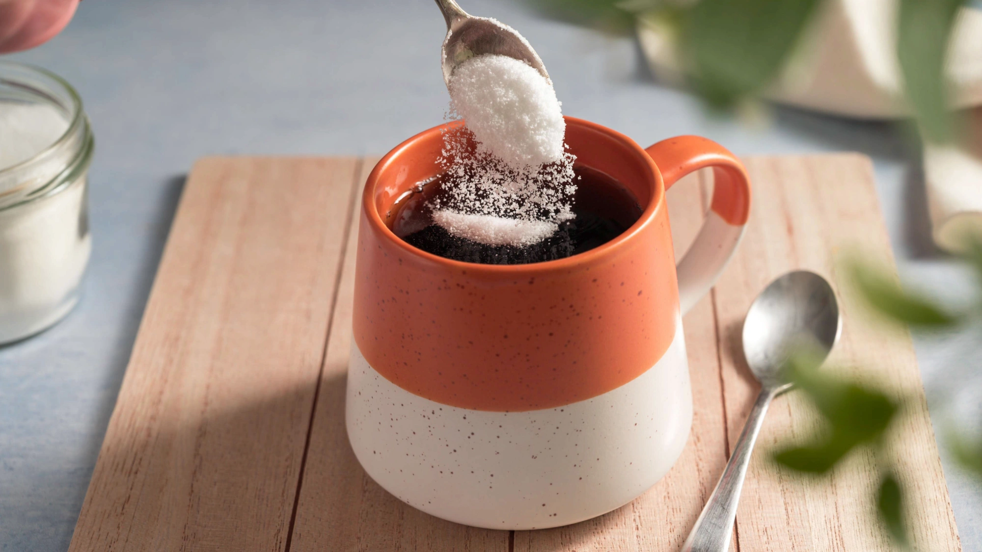 A person adding a packet of sugar-free sweetener into coffee