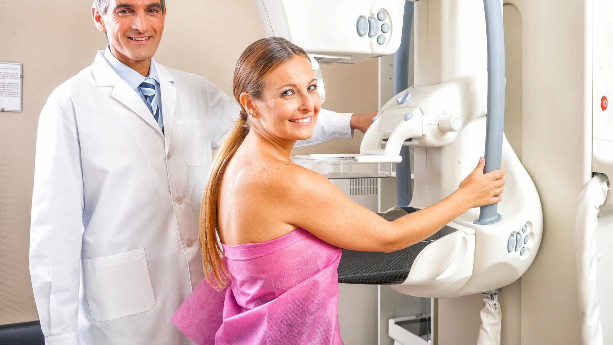 Woman in a pink gown at a mammogram machine for her breast screening exam