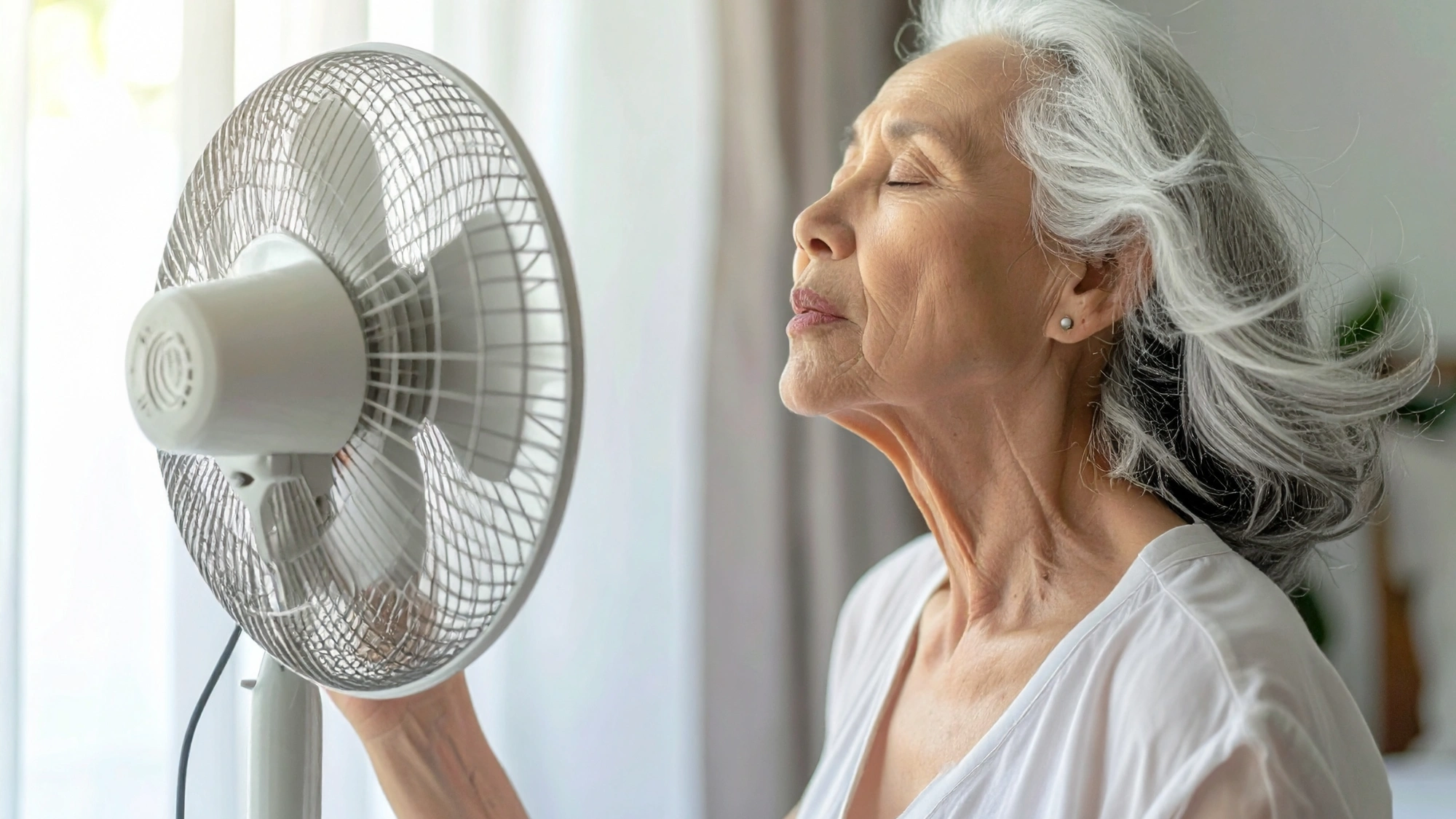 An older woman trying to cool down in front of a fan.