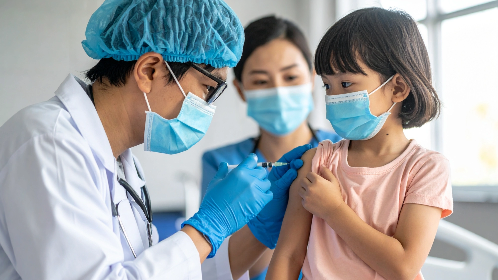 Three nurses in blue scrubs administer a measles vaccine to a young child—highlighting global vaccination efforts to prevent outbreaks like the 2025 U.S. surge.