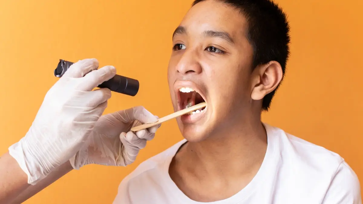 Doctor examines a teen’s throat with a tongue depressor, illustrating evaluation for mononucleosis versus strep throat symptoms.