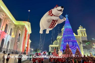 A polar bear balloon wearing a red scarf floats beside a colorful illuminated Christmas tree at the Hollywood Christmas Parade.
