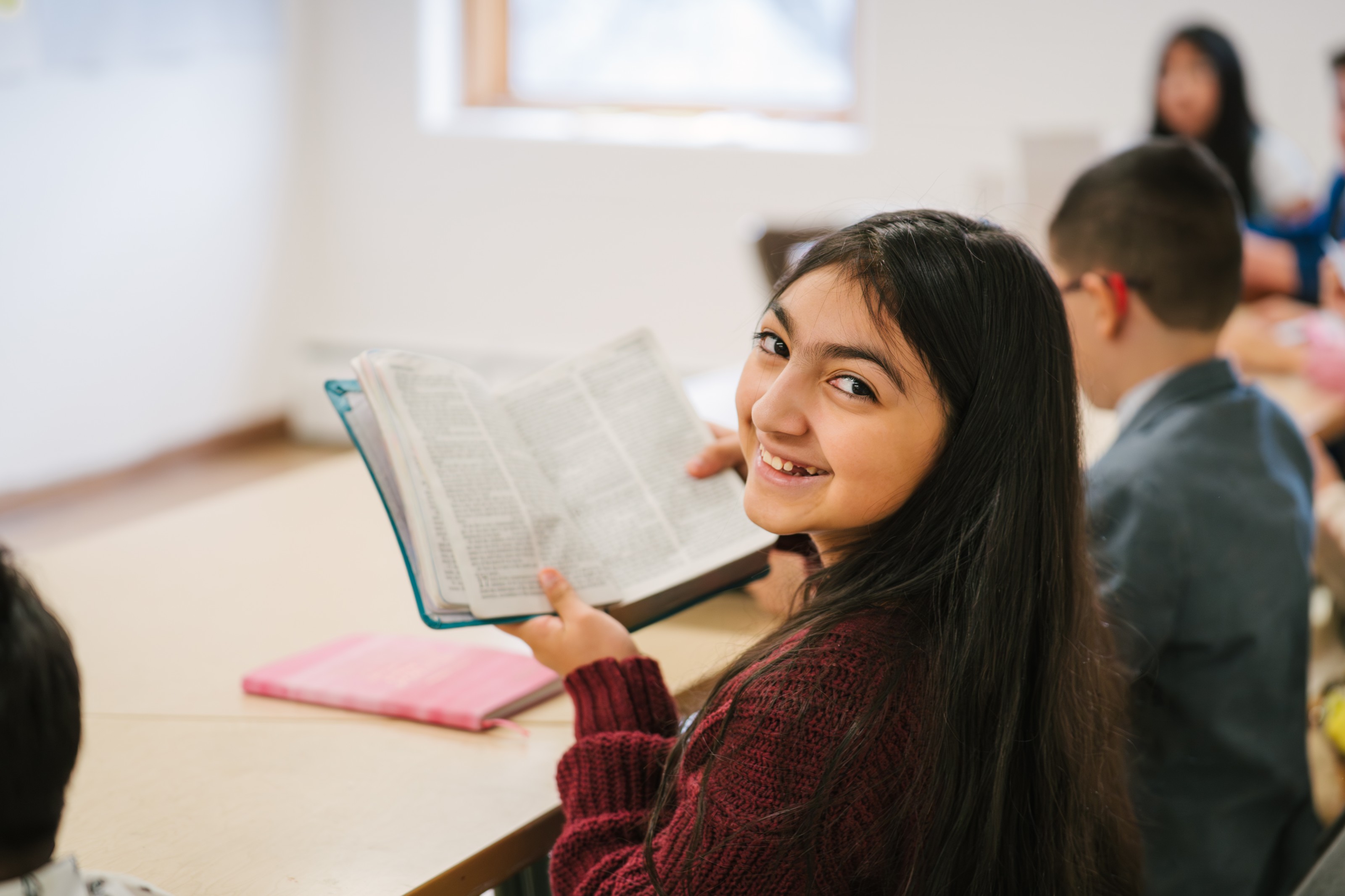Young girl smiling while reading an open Bible in children’s ministry at Voice of Truth Tabernacle