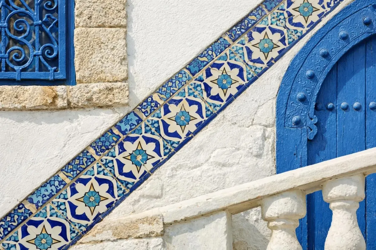Sunny winter street scene in Sidi Bou Said Tunisia with traditional blue and white architecture, Mediterranean coastline view, tourists walking under clear blue sky, warm afternoon light