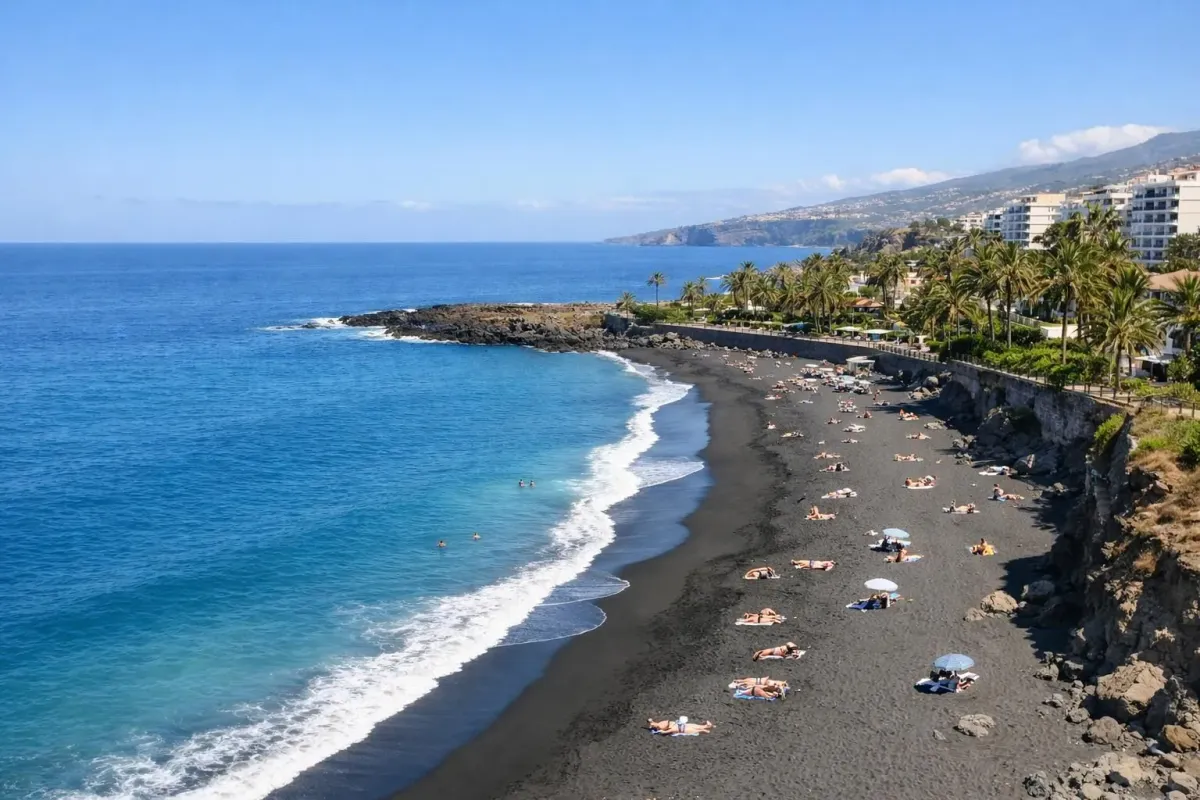 Plage de sable noir volcanique aux Canaries avec océan turquoise et ciel bleu dégagé, quelques palmiers en arrière-plan, destination ensoleillée pour voyager en hiver pas cher