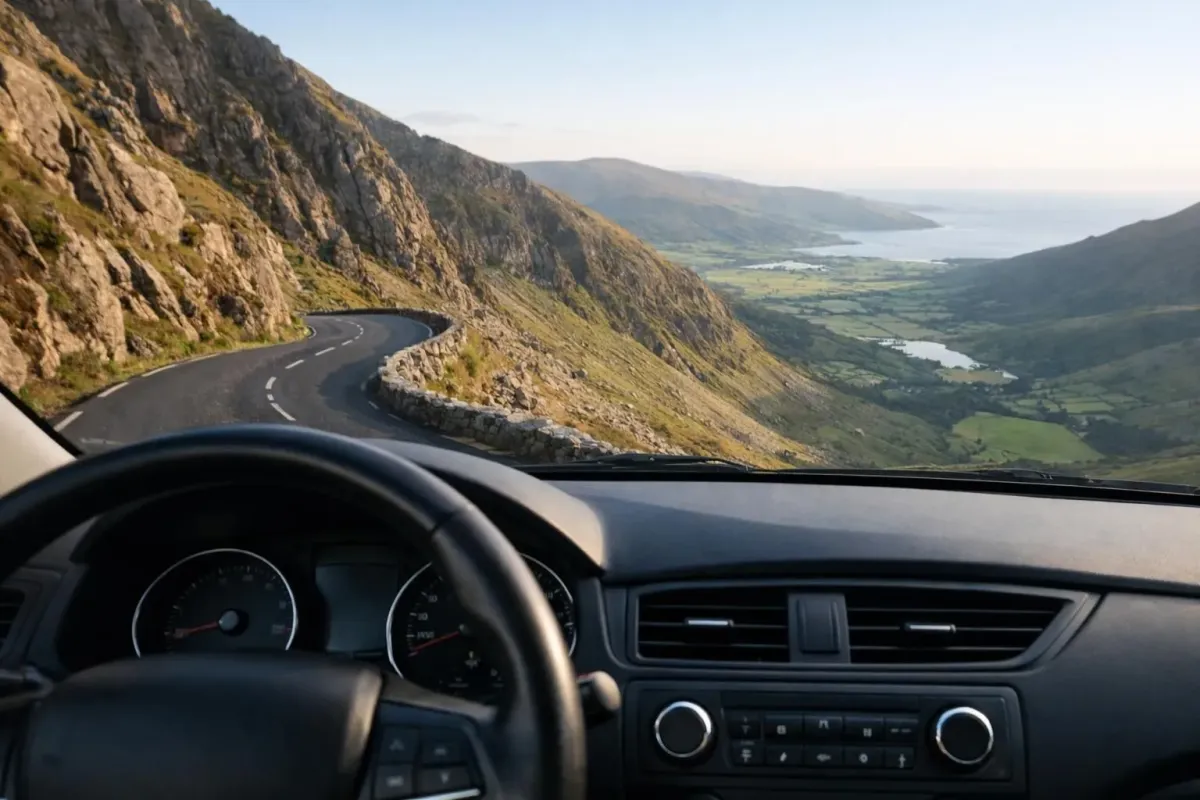 Winding mountain road through Connor Pass in Ireland, dramatic rocky cliffs and green valleys below, morning light casting shadows across the landscape, a single car parked at a viewpoint, wild rugged terrain of the Dingle Peninsula, atmospheric Irish mountain scenery