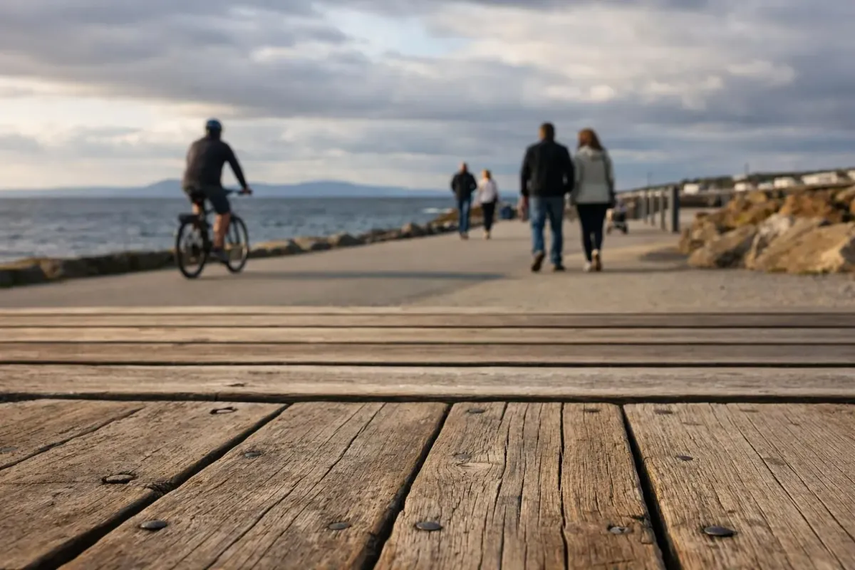 Salthill promenade walkway along Galway Bay with locals walking, cyclists, and the Atlantic Ocean stretching to the horizon under partly cloudy Irish skies