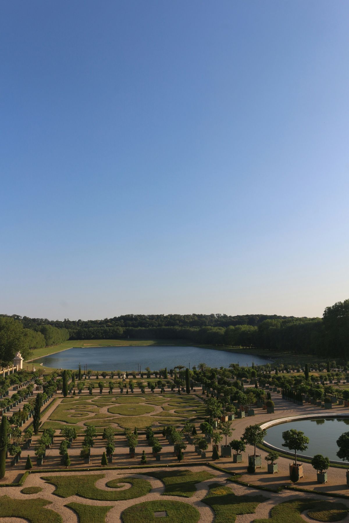 Serene view of the Versailles gardens and the Grand Canal at sunset with few tourists Vue paisible des jardins de Versailles et du Grand Canal au coucher de soleil avec peu de visiteurs