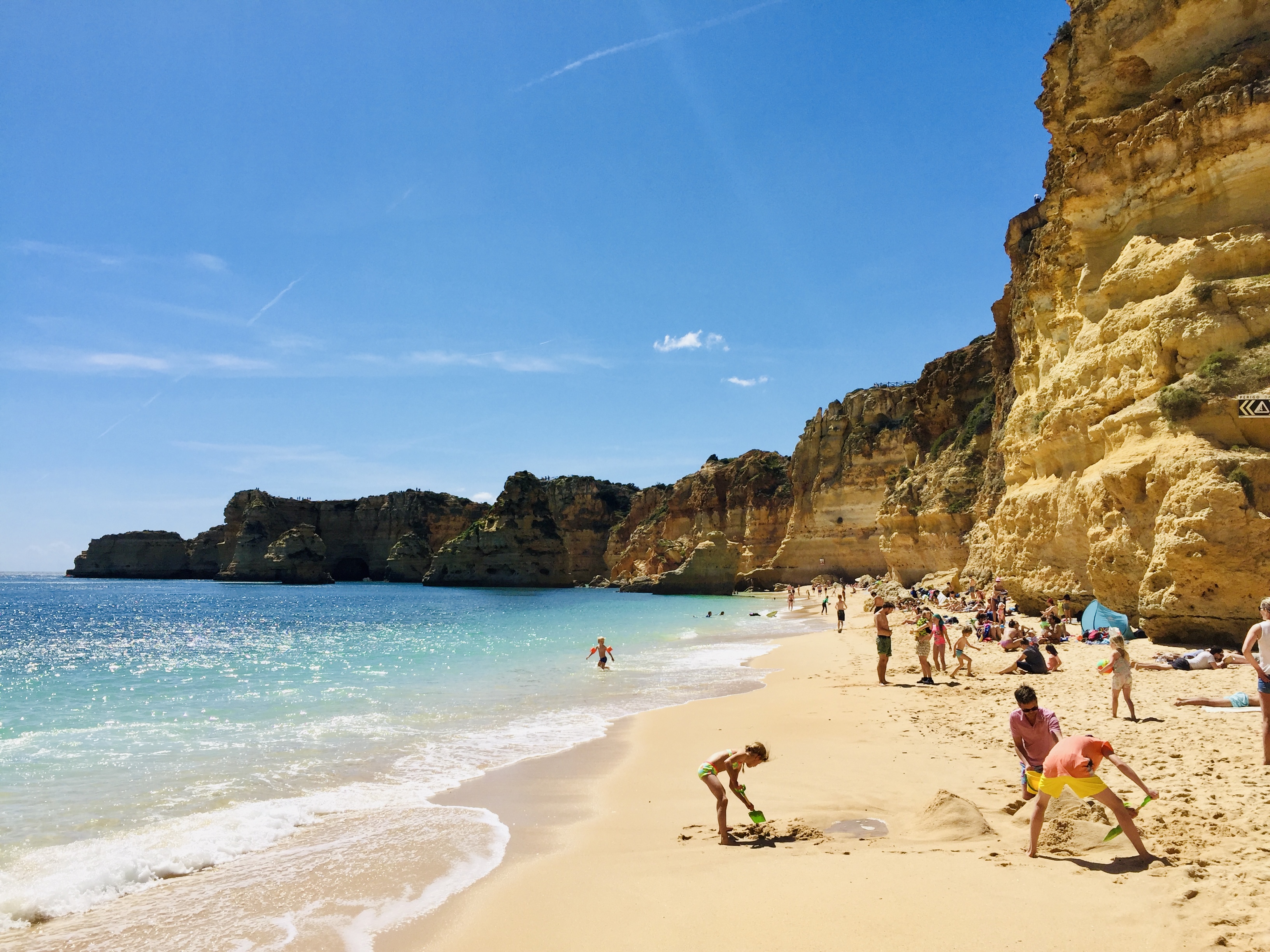 Falaise rocheuse dominant la plage de Marinha au Portugal, avec sable doré et eaux turquoise sous un ciel dégagé