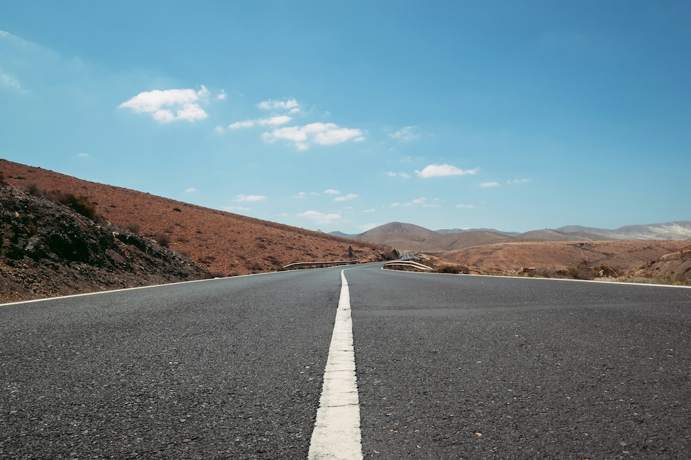 Route sinueuse à travers les paysages dorés d'Espagne lors d'un road trip, avec Madrid en arrière-plan sous un ciel lumineux