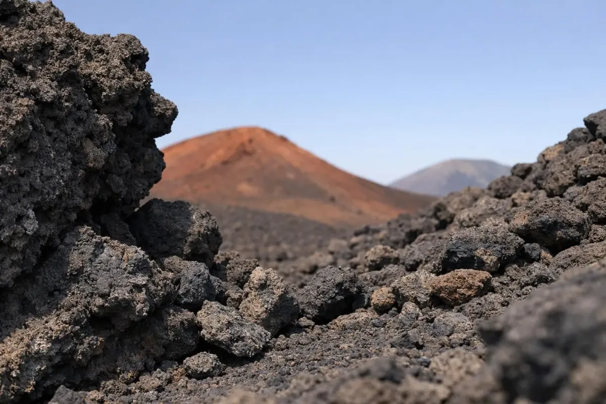 Paysage volcanique escarpé avec une montagne rougeâtre lointaine.