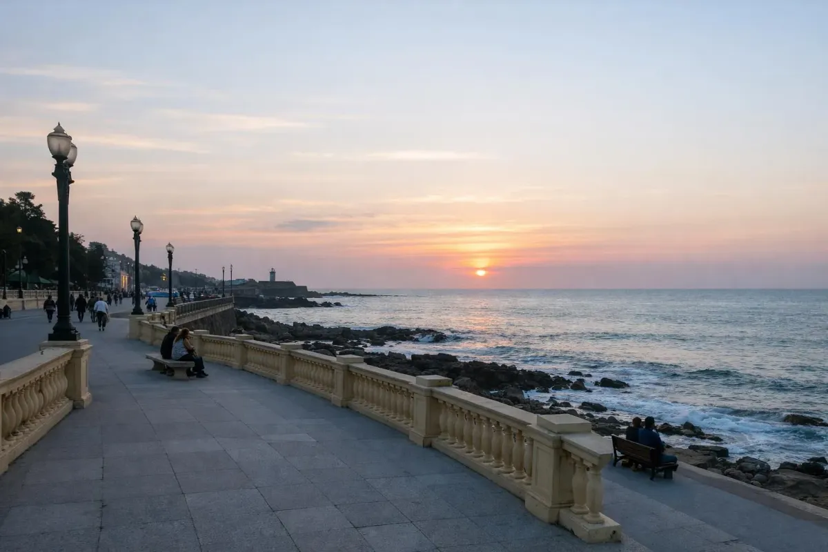 Promenade côtière au coucher de soleil, avec vue sur l'océan et la ville.