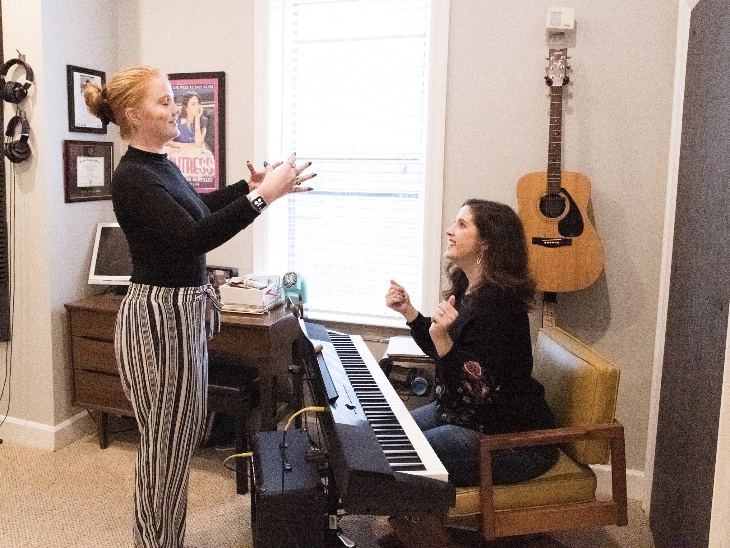 Vocal coach Amber sits at a piano while enthusiastically helps an online vocal client reach their potential