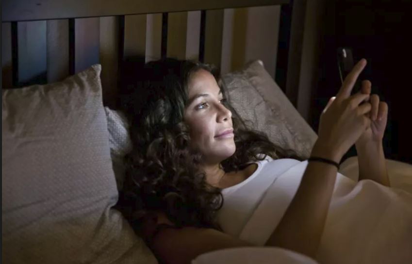 image of women checking phone on the bed