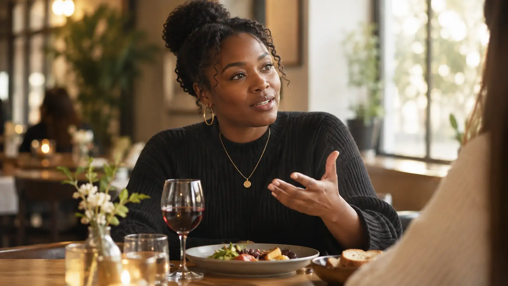 a person at a restaurant table with a small glass of wine in front of them, surrounded by a thoughtful meal, mid-conversation gesture