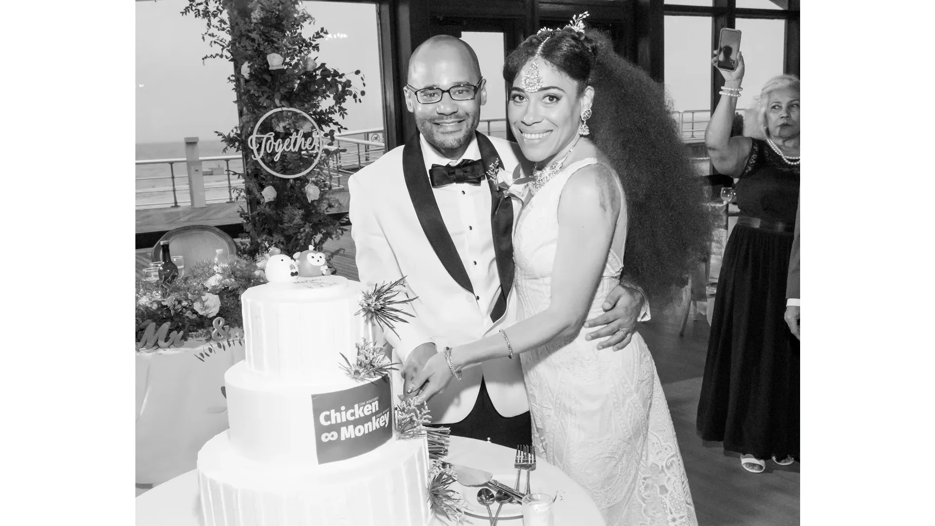Joe and Rosa standing together in front of their wedding cake, smiling for a photo