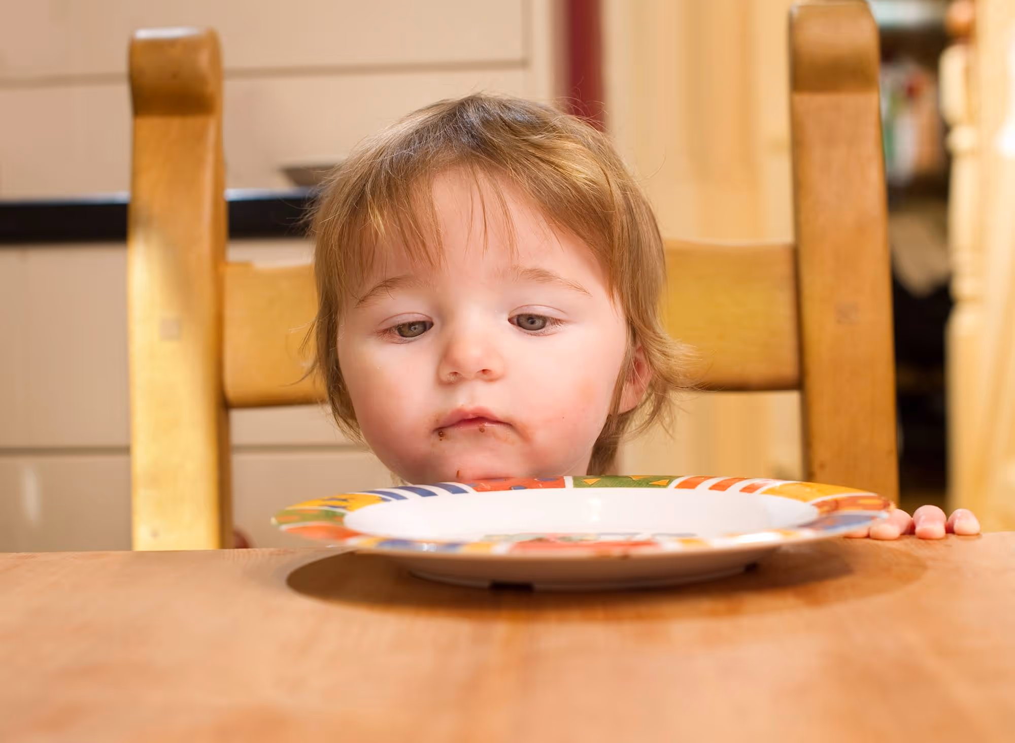 a beautiful little girl stares at her empty plate