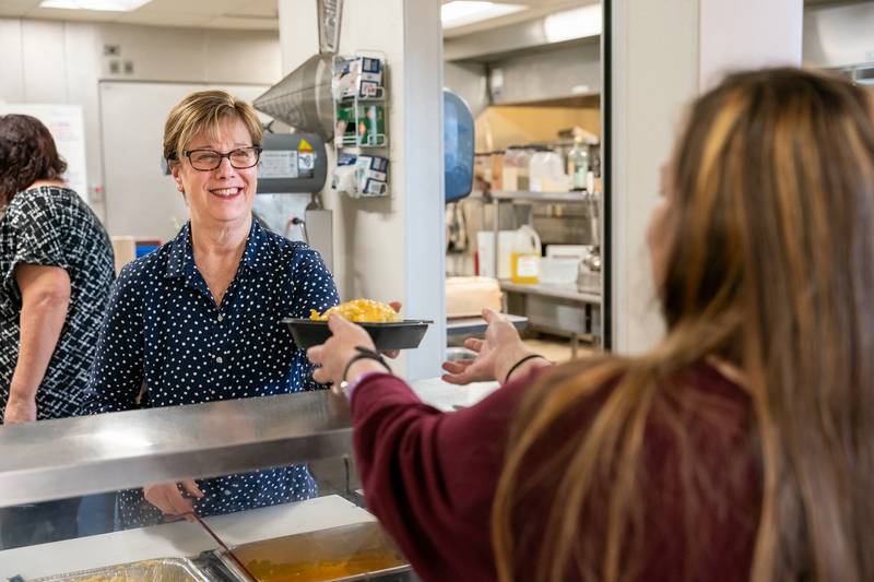 A female resident gives a big smile while sitting at a table in the cafeteria eating breakfast