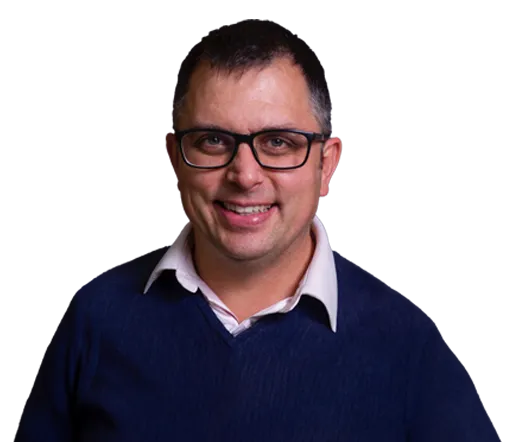 Smiling man wearing black glasses, a white collared shirt, and a navy blue sweater.