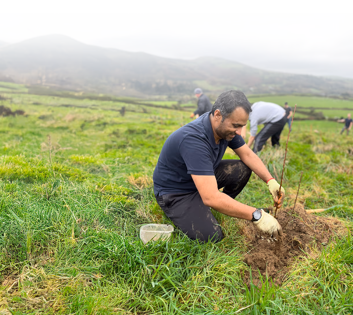 A Capital International team member tree planting in a field with colleagues