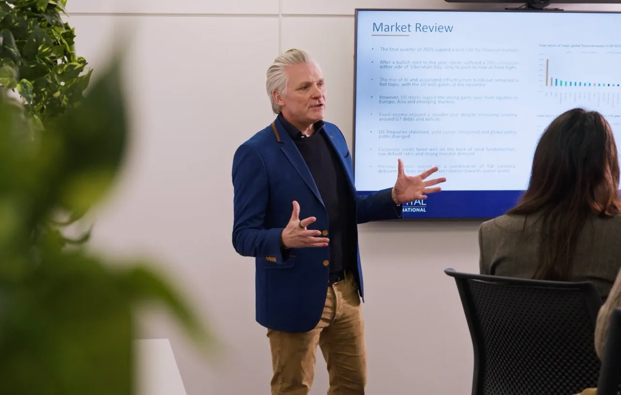 Man in blue blazer giving a market review presentation to an audience in a conference room.