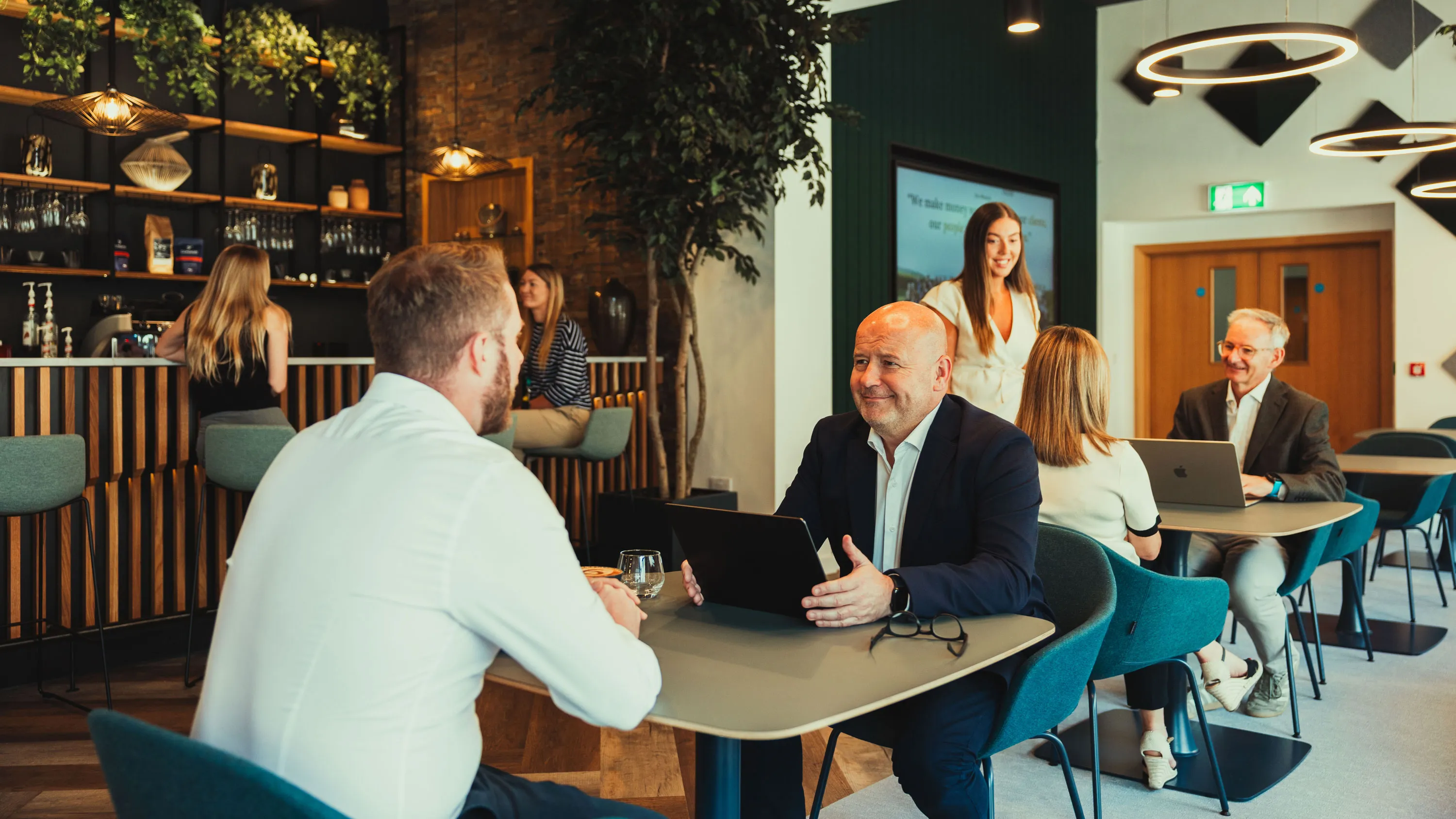 People engaged in meetings and conversation at tables in a modern office cafe setting.
