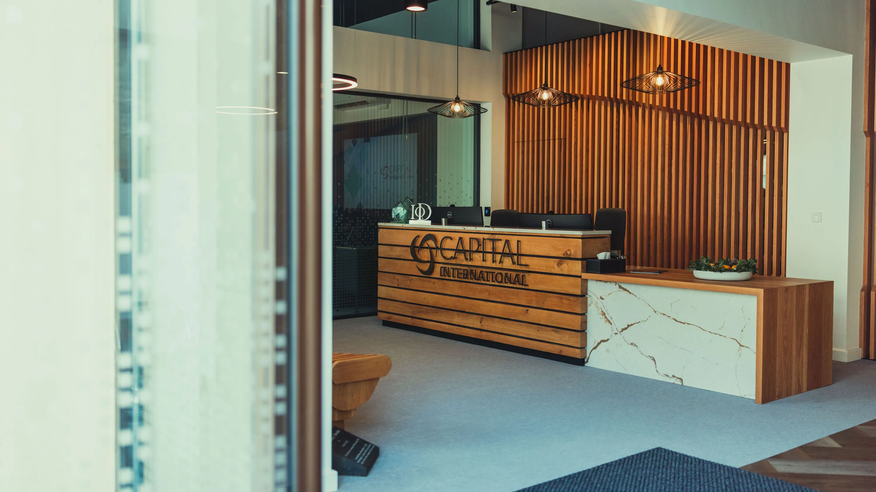 Modern office reception with wood panel desk, marble side, and hanging pendant lights.