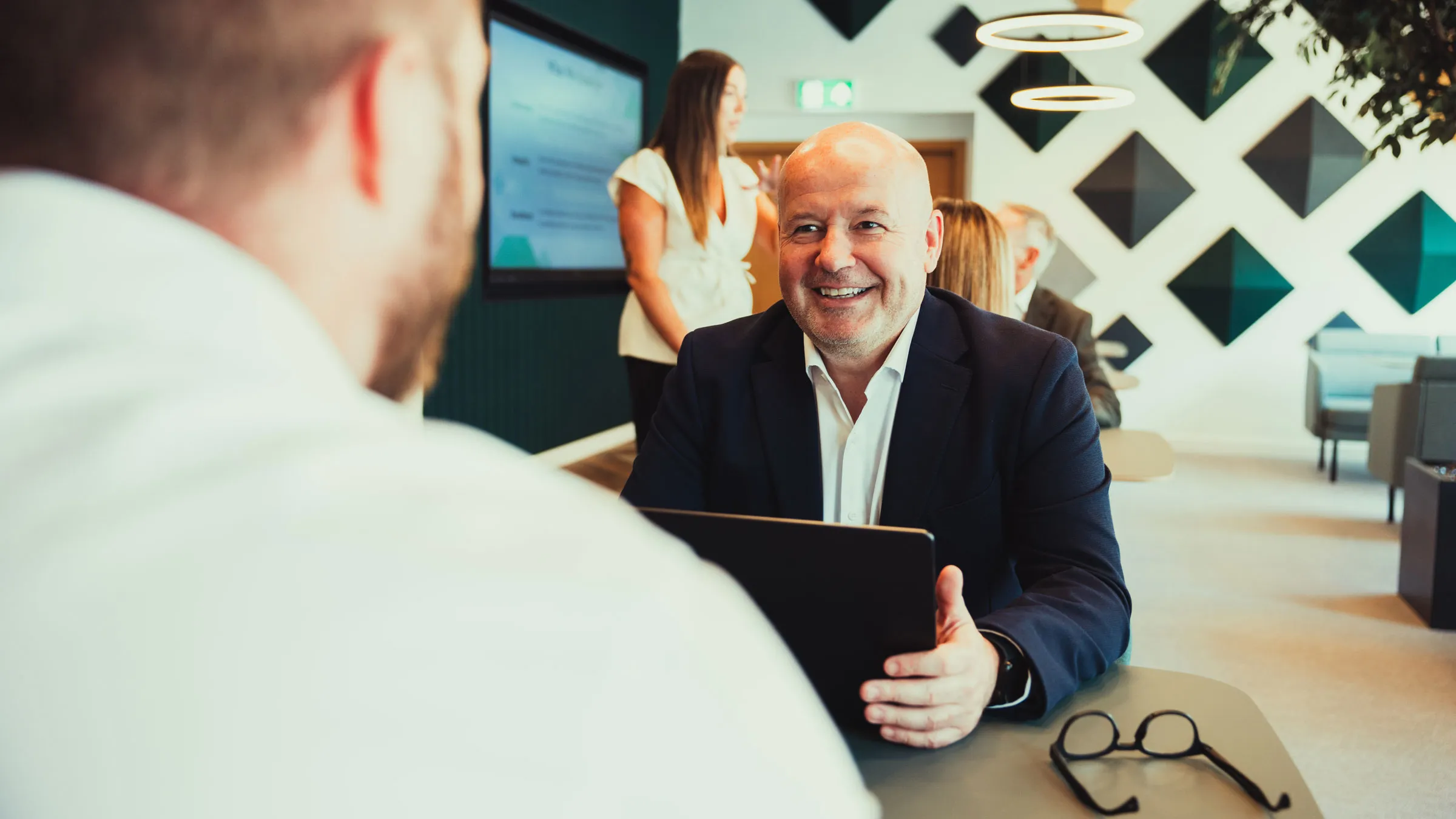 Smiling man in suit talking to a person in a white shirt in modern office setting.