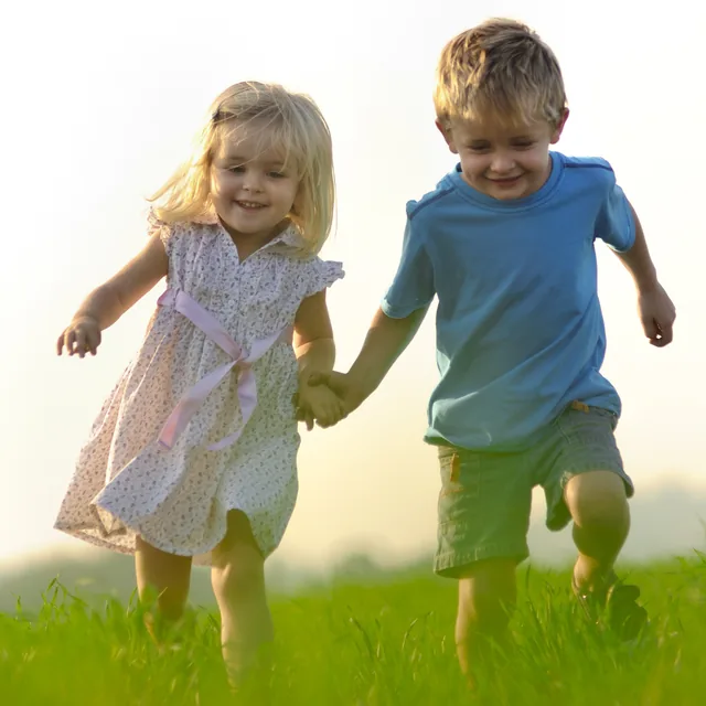 Junge und Mädchen laufen Hand in Hand über eine Wiese – Thema Partnerschaft
