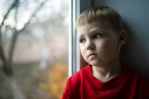 Trauriger Junge im roten Pullover schaut aus dem Fenster