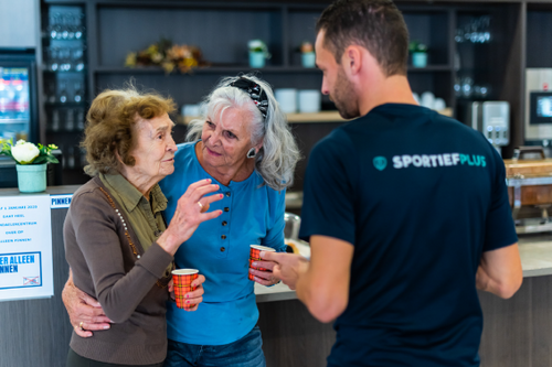 Twee oudere dames worden ondersteund door een sportleraar