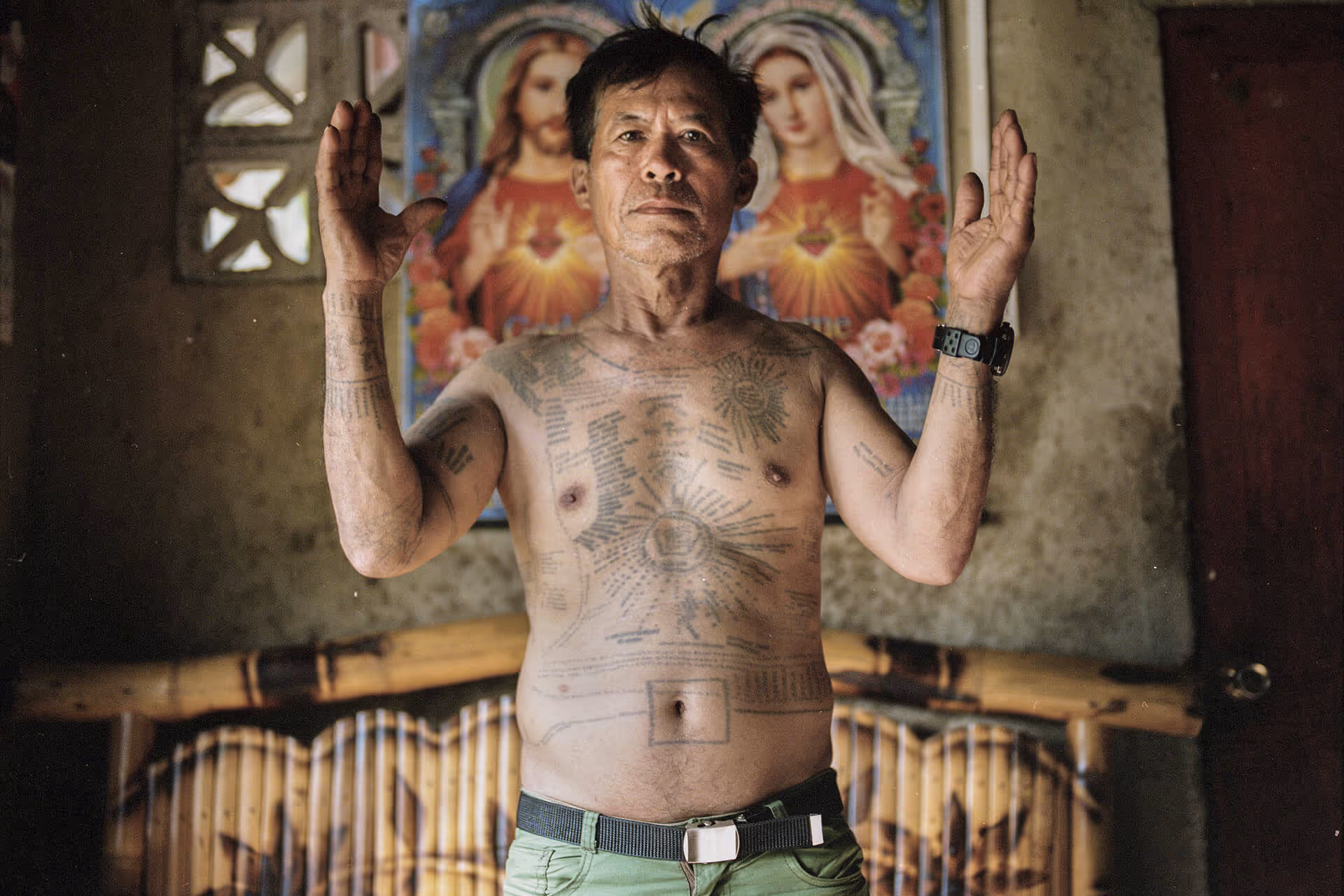 Quirino Ponce poses with his tattoos in front of a staple Filipino Catholic calendar in his home in Siquijor, photo by Geric Cruz
