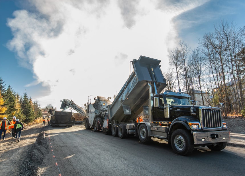 Foreman and contractor on roadworks site reviewing information on a tablet surrounded by traffic cones and equipment & Civil construction contractors measuring the thickness of freshly laid pavement.