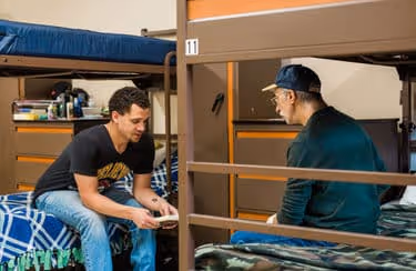 Two male residents sit on bunks opposite each other having a discussion