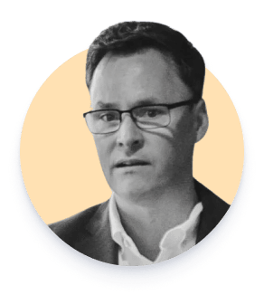 Hombre con gafas y chaqueta mirada hacia adelante sobre fondo amarillo claro.