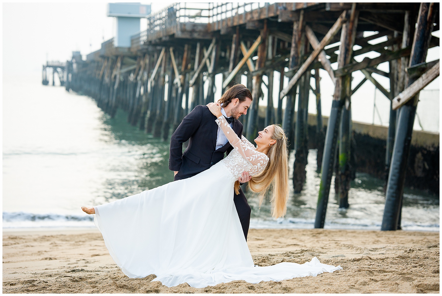 Romantic Seal Beach engagement portraits with a second-hand white dress, fitted white gown, and classic black suit. Coastal wedding photography with playful movement.