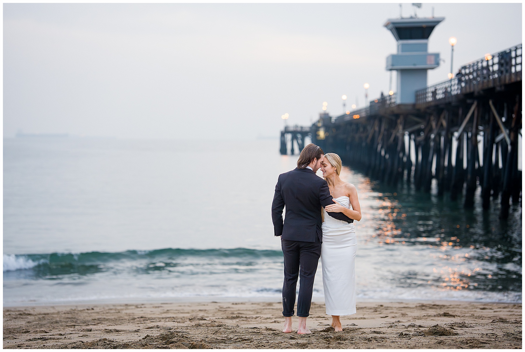 Romantic Seal Beach engagement portraits with a second-hand white dress, fitted white gown, and classic black suit. Coastal wedding photography with playful movement.