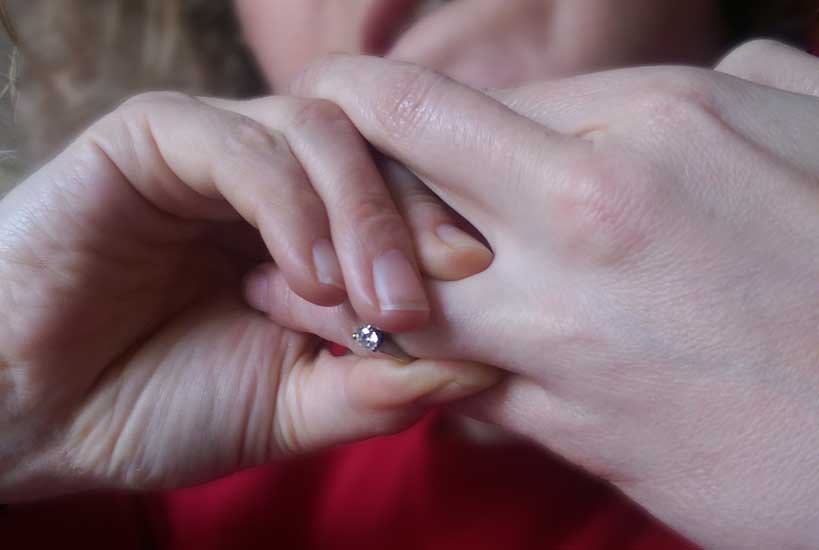 Close-up of a diamond engagement ring being placed onto a finger