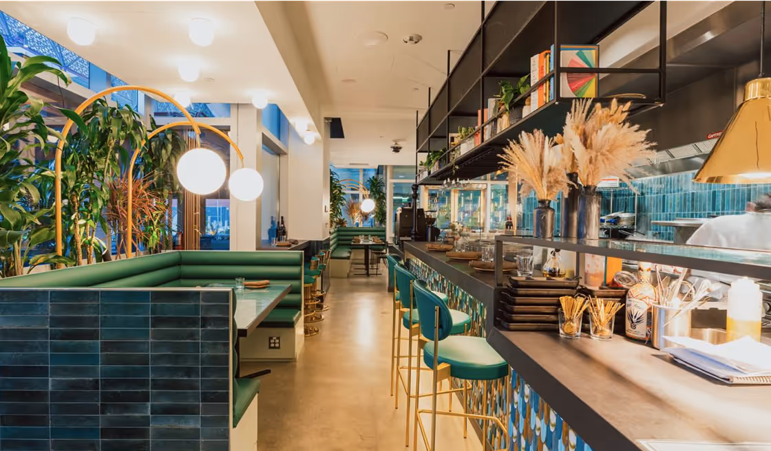 A restaurant with a long counter and green chairs.