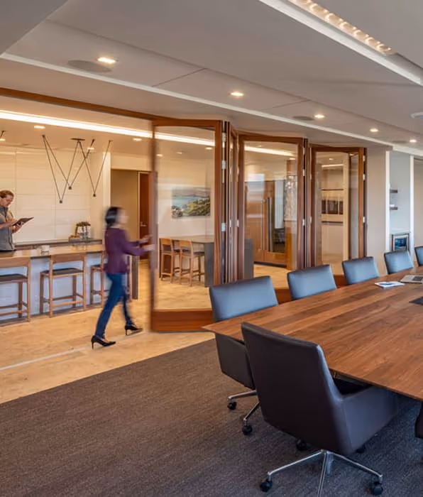 Modern conference room with large wooden table, black chairs, and glass walls with wooden frames.