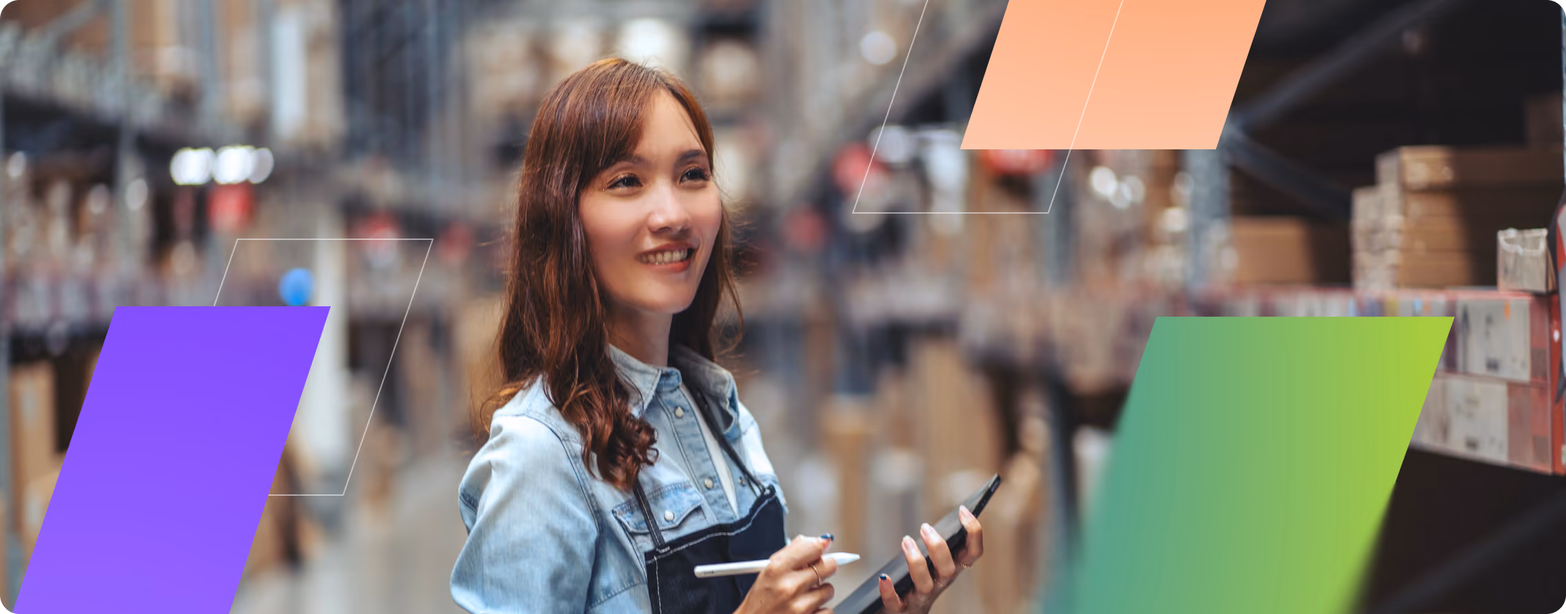 Smiling woman in denim shirt and apron holding stylus and tablet in a warehouse aisle.