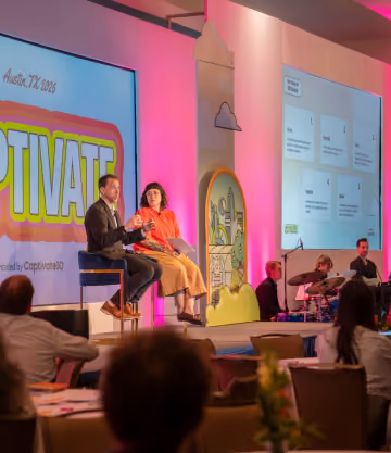 Two speakers seated on stage in front of a screen with CaptivateIQ branding at an event in Austin, TX.